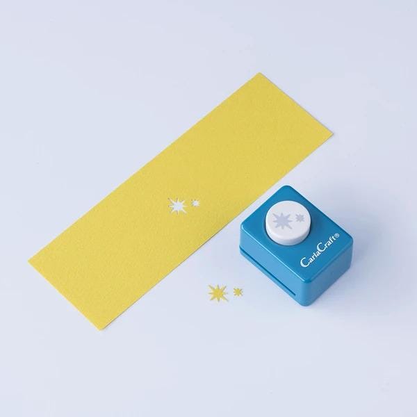 a yellow paper with small white star-shaped cutouts and a blue paper punch with a white star-shaped cutout on it, both placed on a white background.