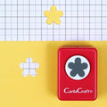 A red hole puncher with a black flower design on it, placed on a yellow background with a grid pattern.