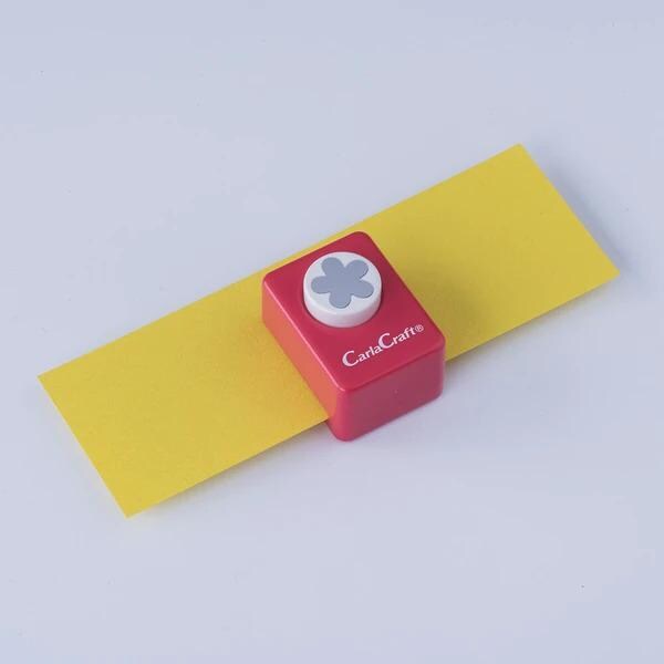 A red and yellow paper punch with a white flower design sits on a yellow piece of paper against a white background.