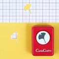 A red hole puncher with a black and white ginkgo leaf design on it, placed on a yellow background with a grid pattern.