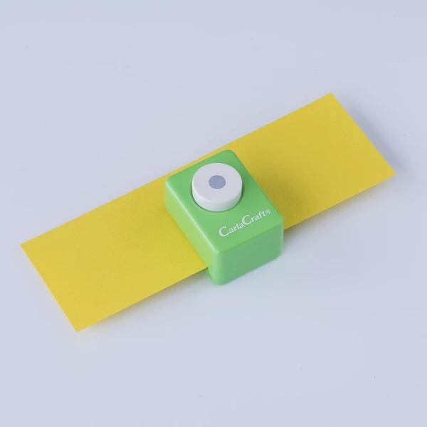 A green and white hole puncher is placed on a yellow piece of paper against a white background.