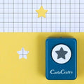 A blue hole punch with a star-shaped hole in the center is shown on a yellow background, with a grid pattern visible in the background.