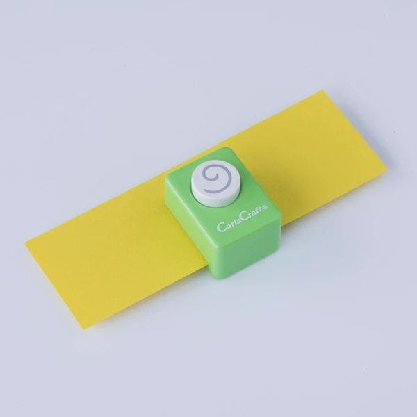 A green push button cutter with a white spiral design on it, placed on a yellow surface.