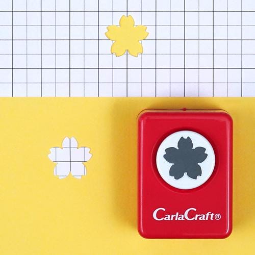 a red hole puncher with a black and white flower design on it, placed on a yellow background with a grid pattern.