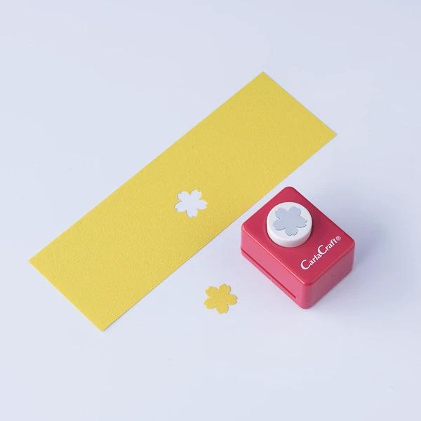 a yellow paper with two white flower-shaped cutouts and a red paper punch with a white flower-shaped cutout on top.