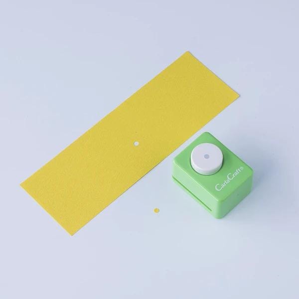 a yellow paper and a green paper punch on a white background.