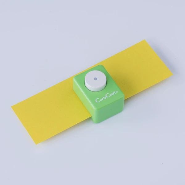 A green and yellow paper cutter is placed on a yellow piece of paper against a white background.