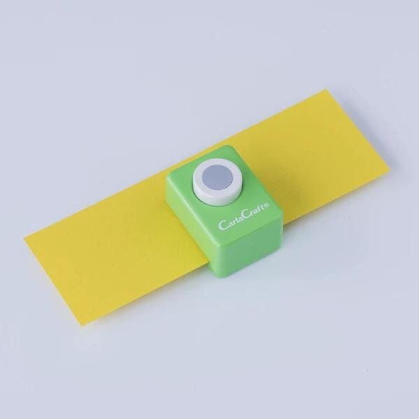 A green and white card crafting tool is shown on a yellow piece of paper against a white background.