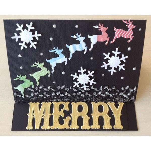A handmade Christmas card with a black background, featuring a festive scene with reindeer and snowflakes. The word "MERRY" is prominently displayed in the foreground.