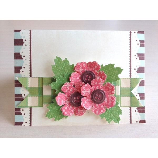 A handmade card with a floral design and decorative elements, including a large pink flower with three purple buttons as the centerpiece.