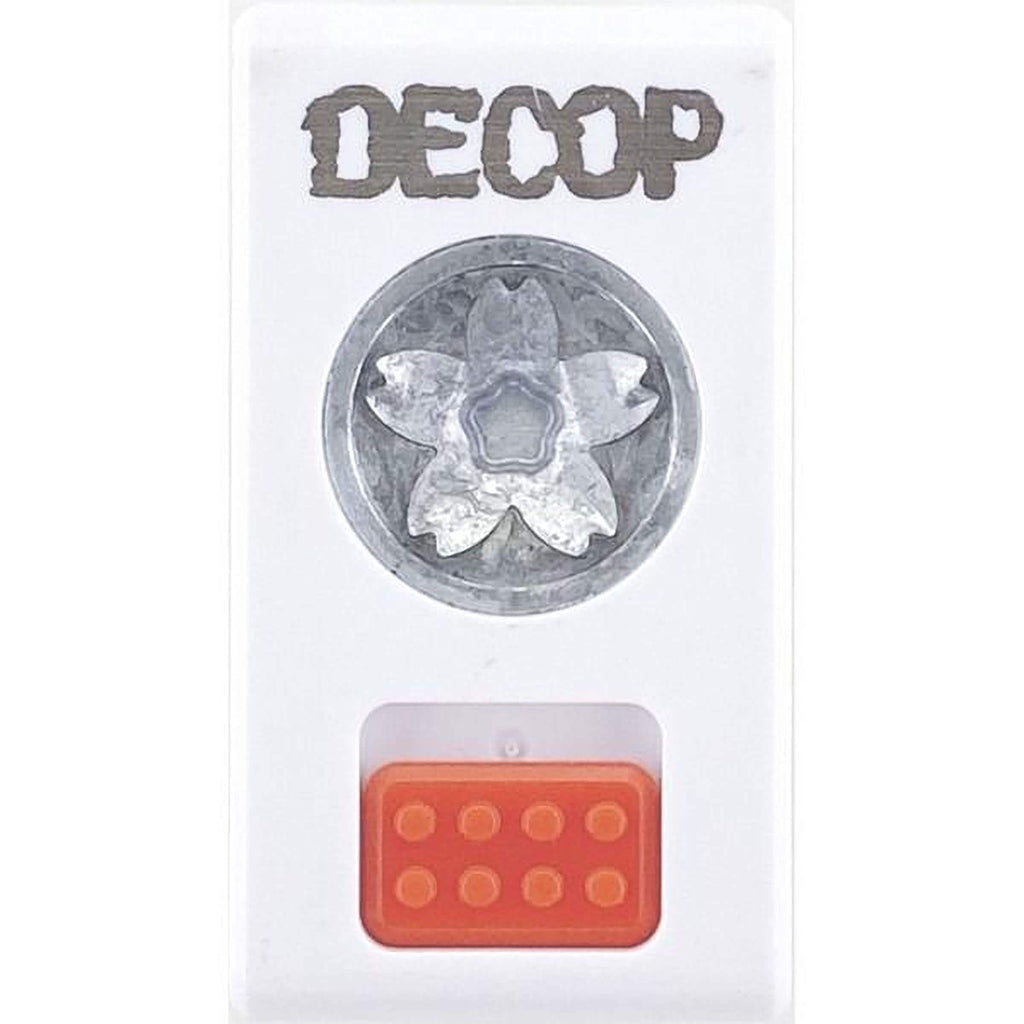 a white plastic container with a silver metal flower design on the front, and an orange plastic object with a red circular pattern on the bottom.