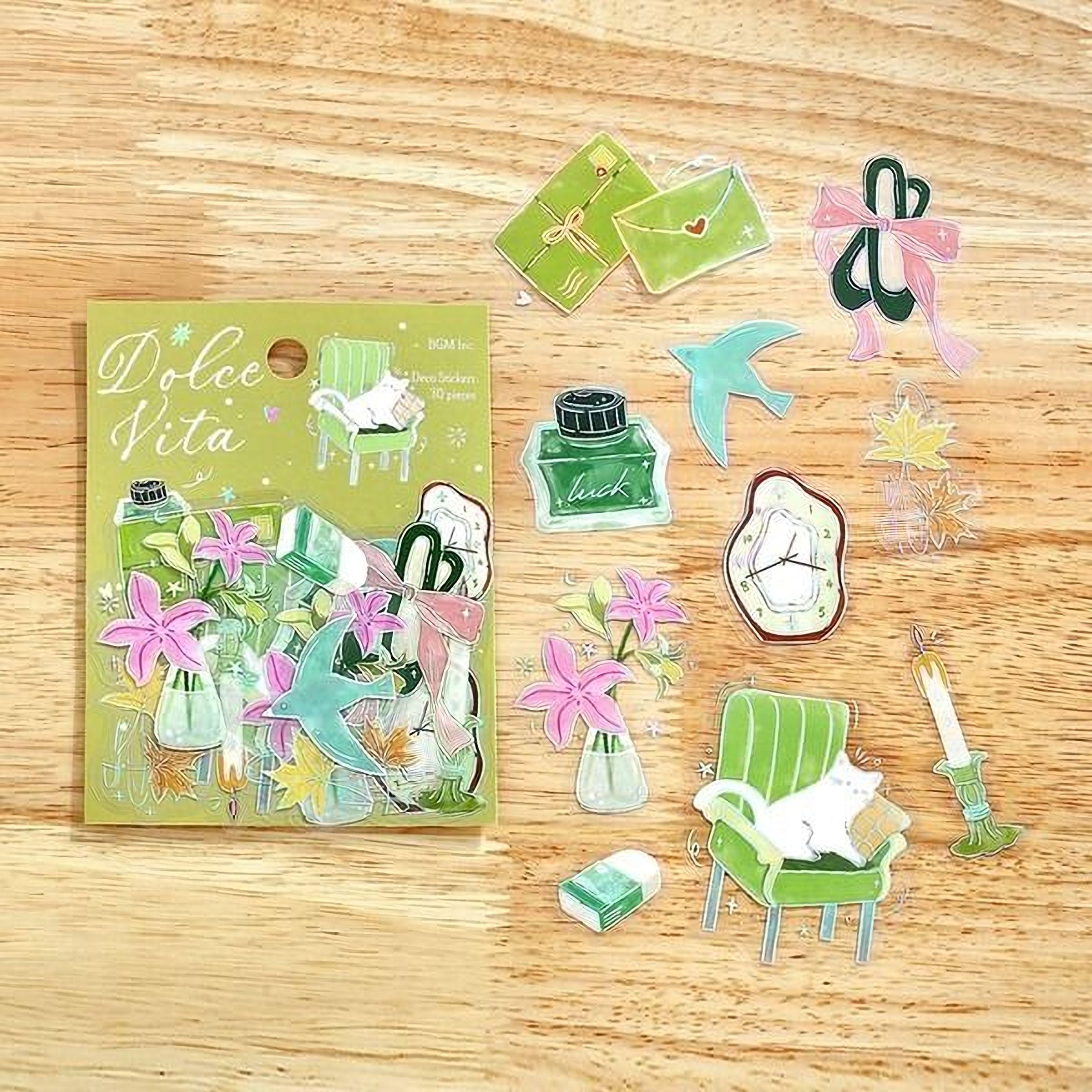 various cut-out stickers and illustrations of objects and scenes, including a green book, a cat, flowers, a clock, and other decorative elements, all arranged on a wooden surface.
