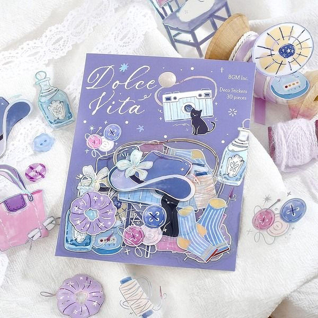 a purple sticker with various decorative elements, such as a cat, flowers, and sewing supplies, surrounded by other craft supplies and a lace doily.