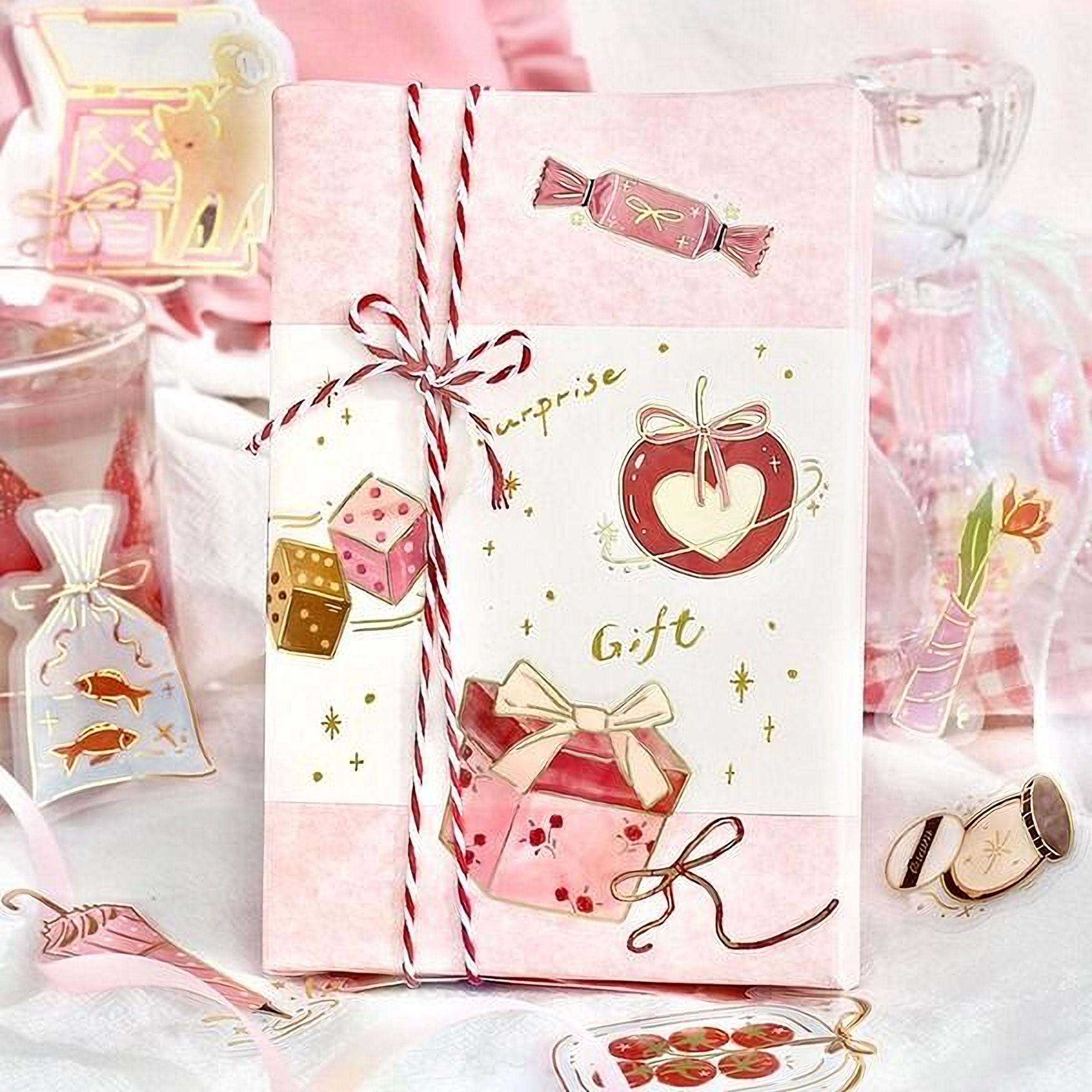 a pink gift box with various decorative elements, including a heart, candy, and other festive items, all wrapped in a pink and white paper.