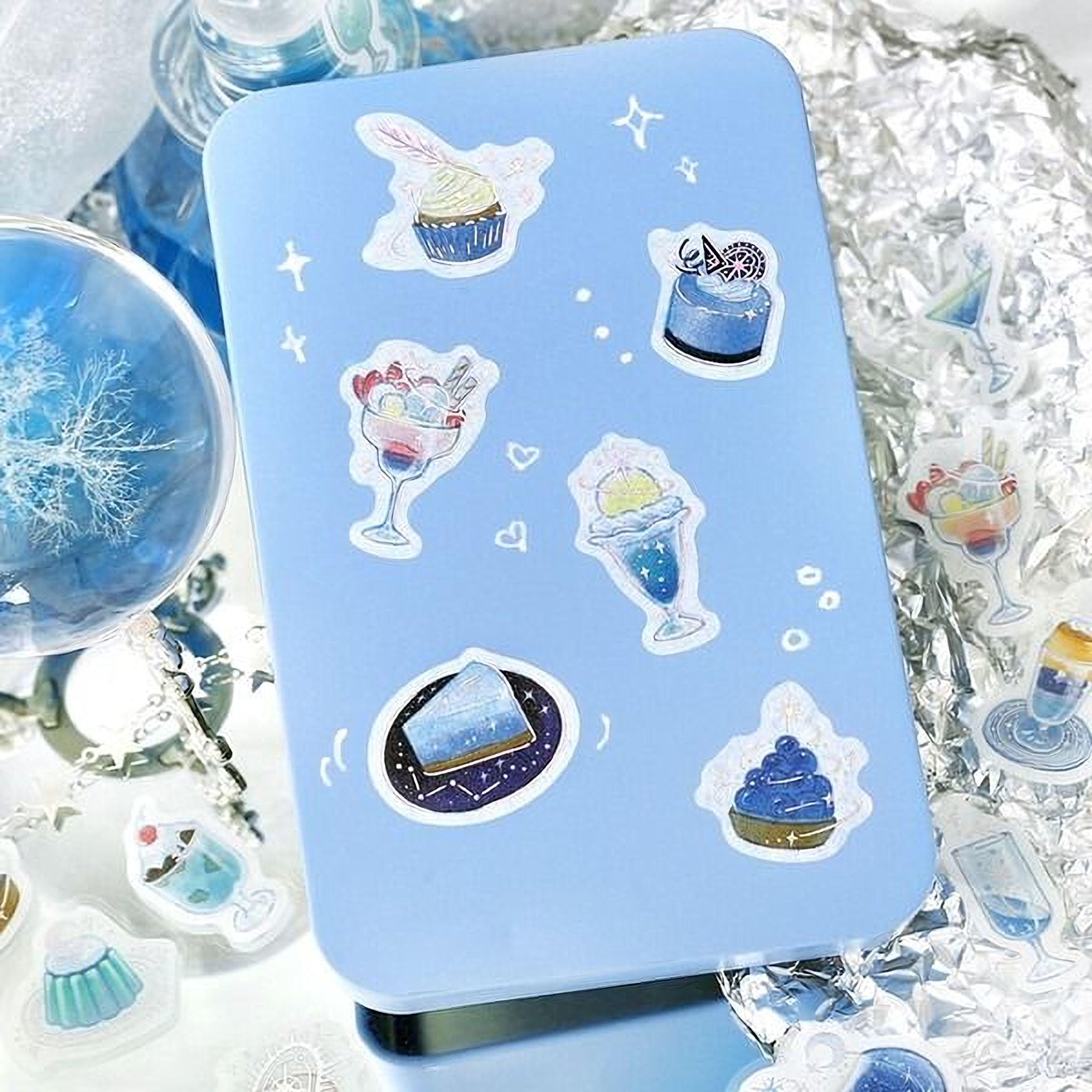 a blue tin with various desserts and drinks depicted on its surface, surrounded by other decorative items such as a snowflake, a glass, and a starry background.