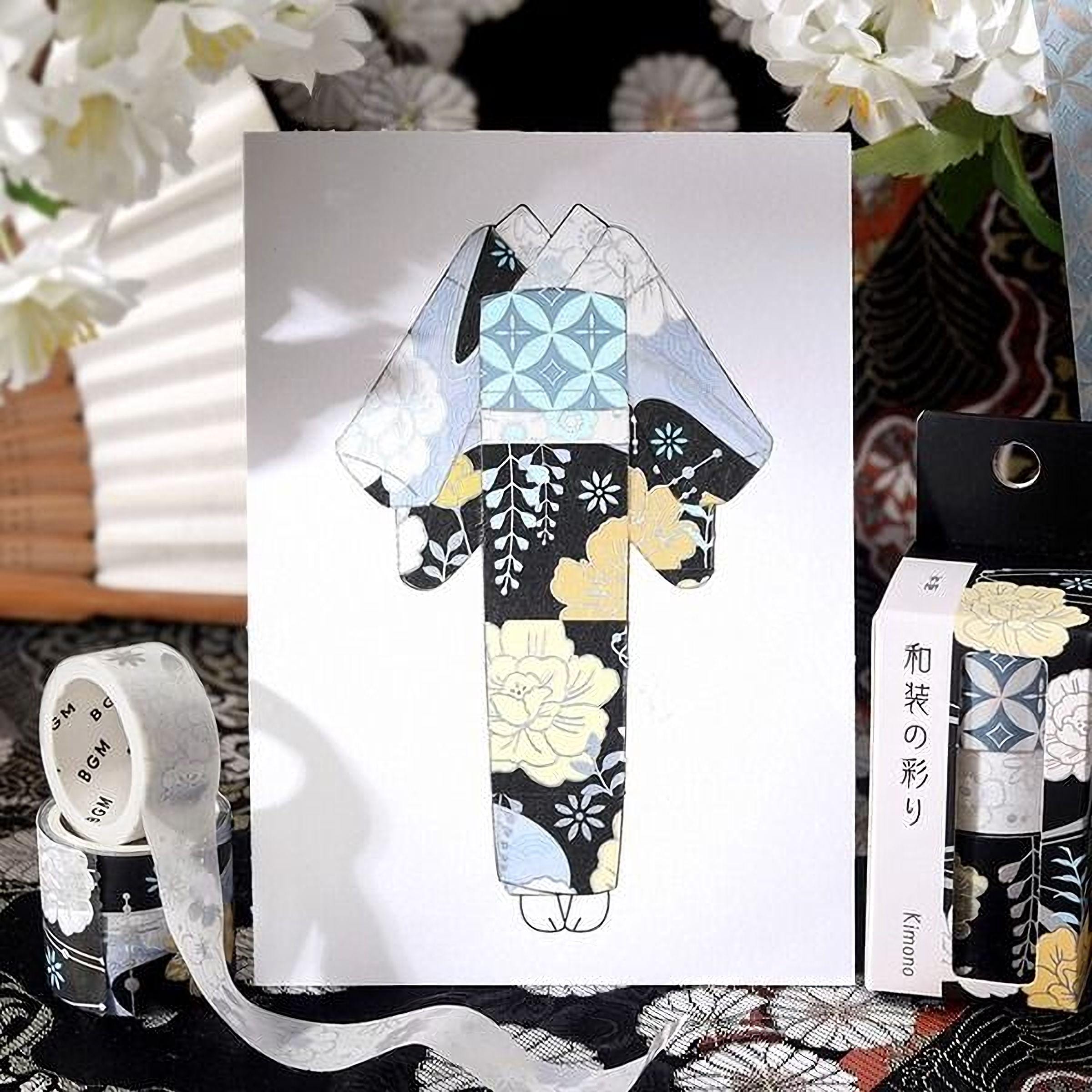 a colorful kimono-style garment with a floral pattern, displayed on a white background. There is also a roll of tape and a book with Japanese text on it, suggesting a cultural or artistic context.