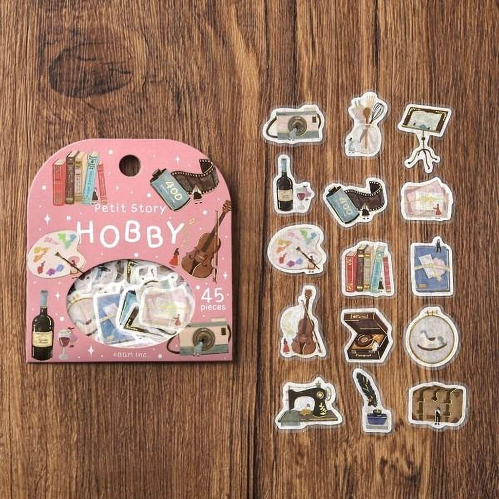 a pink sticker pack with various stickers depicting hobbies, such as books, art supplies, and musical instruments, placed on a wooden surface.