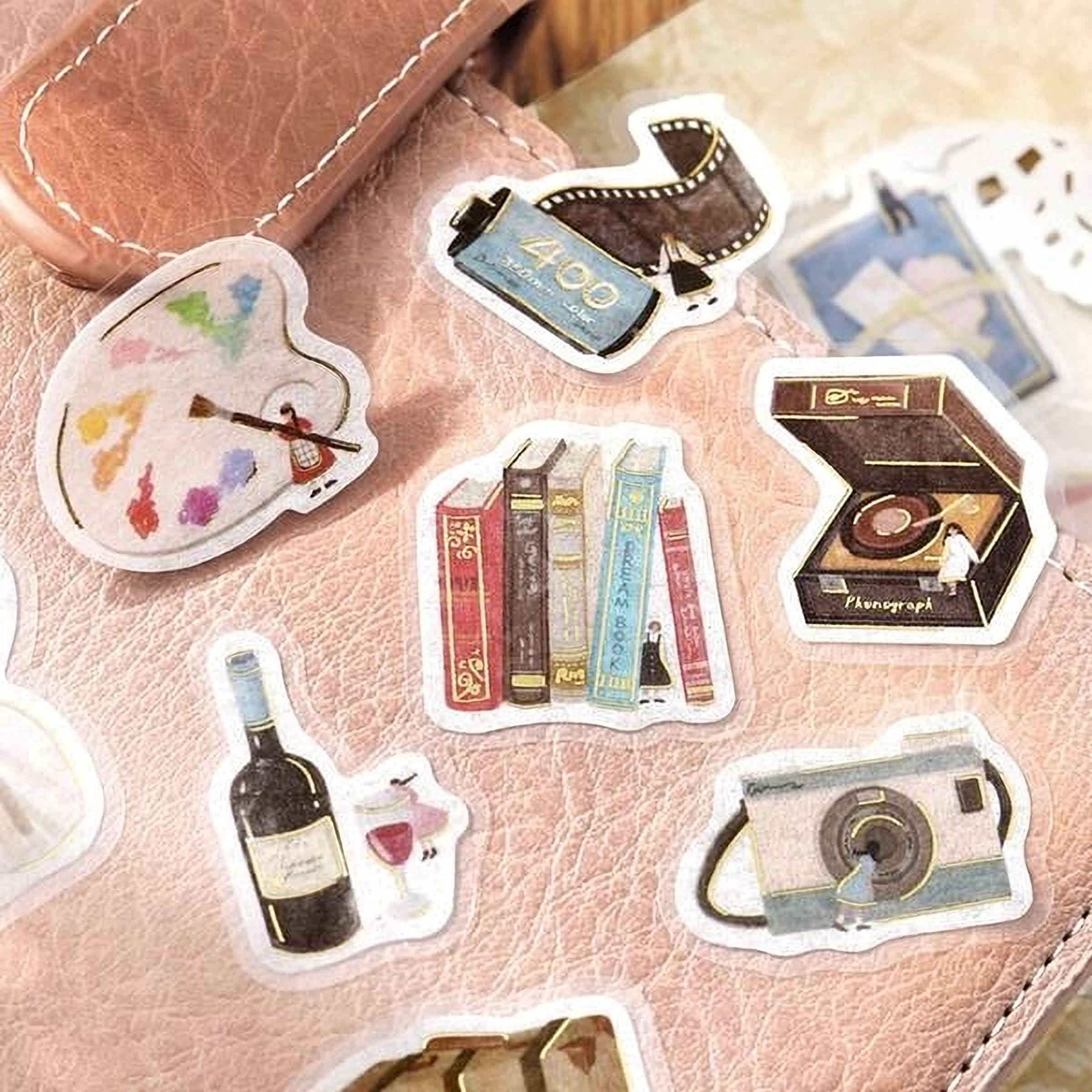 a collection of various stickers, including a paint palette, books, a camera, and other objects, all arranged on a pink surface.