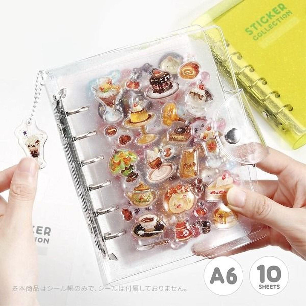 A transparent notebook with various food-themed stickers attached to it, held in someone's hands.