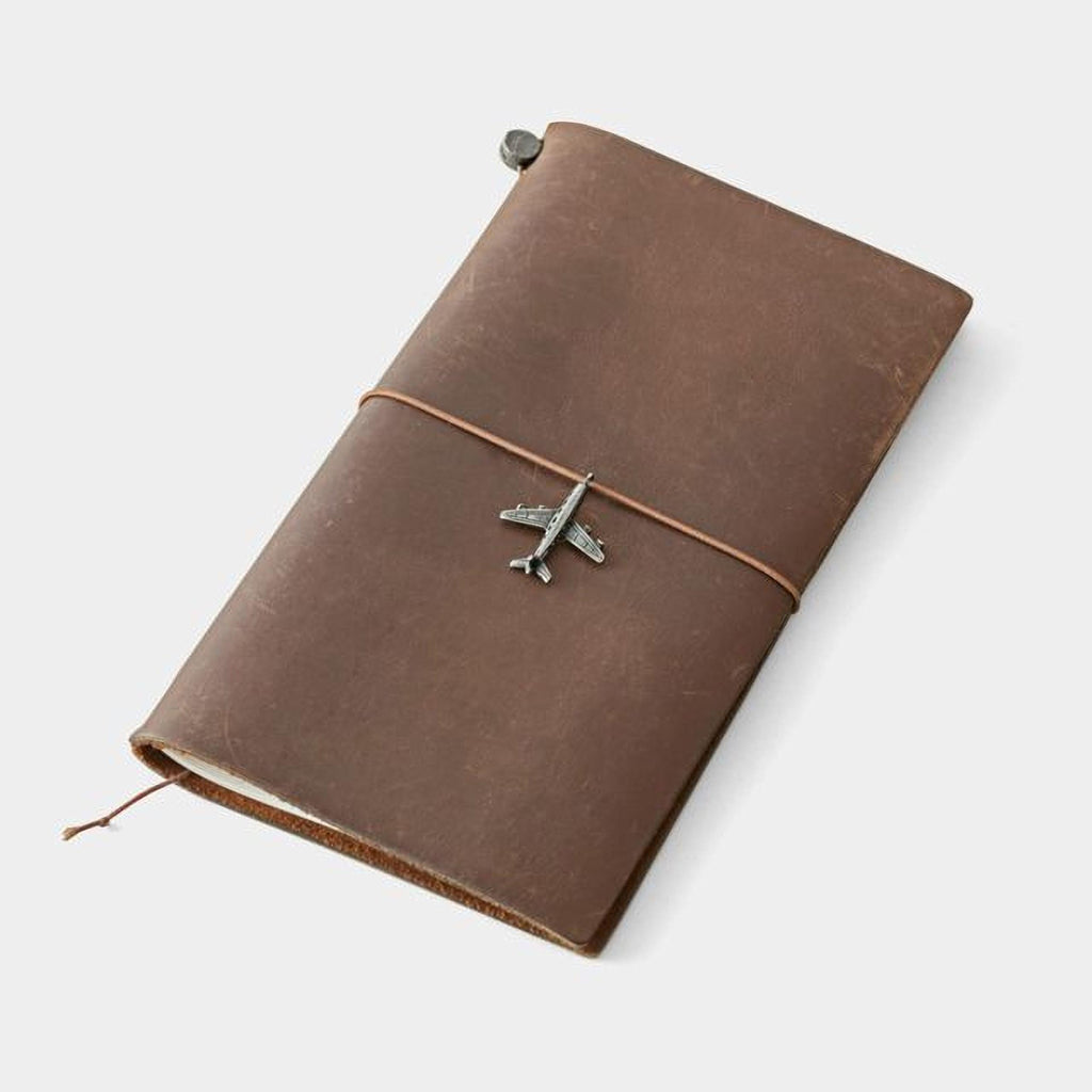 A brown leather-bound notebook with a metal airplane charm on the cover.