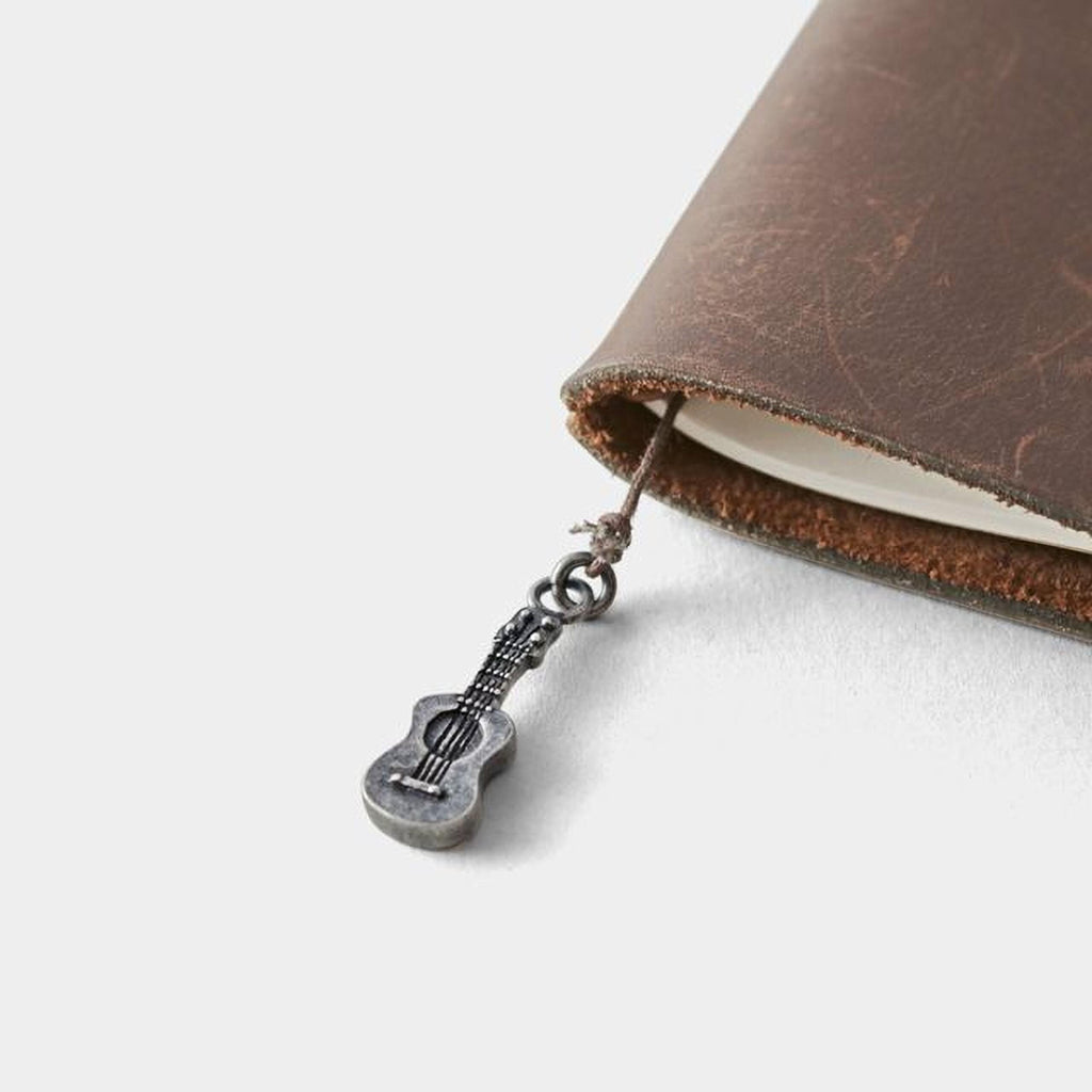 A small silver guitar charm is attached to a leather-bound notebook.