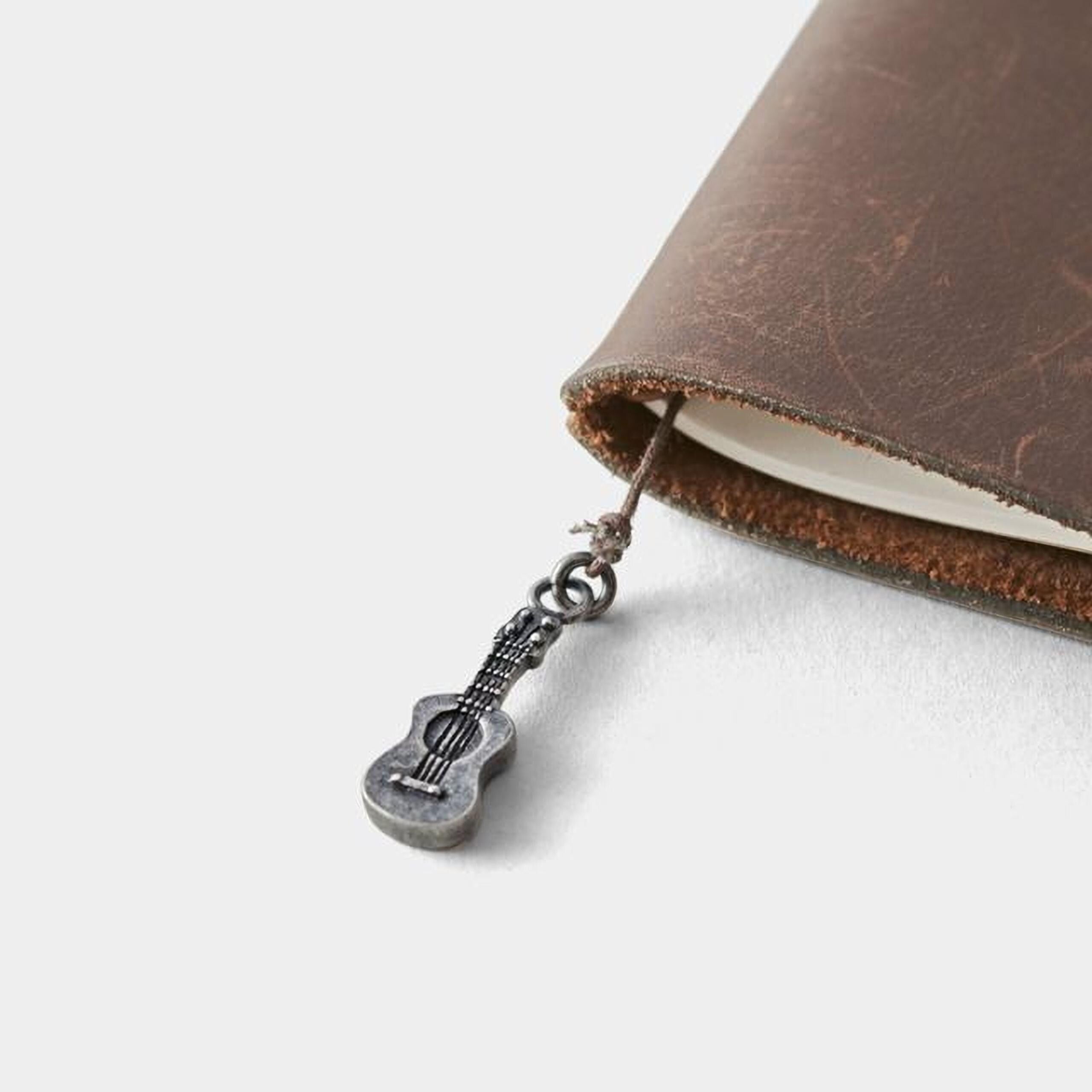 A small silver guitar charm is attached to a leather-bound notebook.