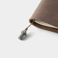 A close-up view of a small metal bolt or nut attached to a leather-bound notebook or journal.