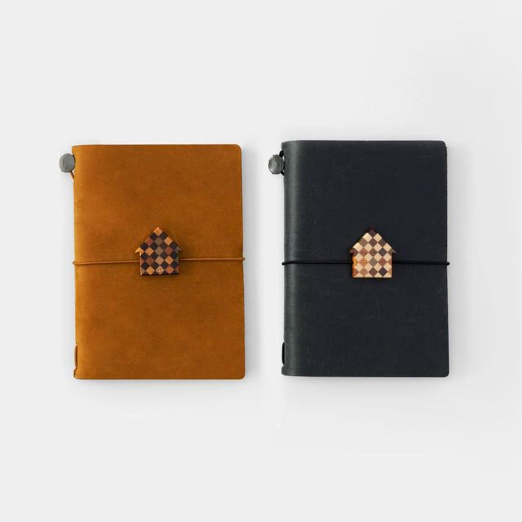 Two notebooks with a checkered house-shaped charm on the cover, one black and one brown.