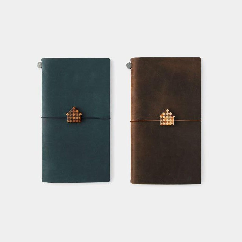 Two leather-bound notebooks with a house-shaped charm on the cover, one in a dark green color and the other in a brown color.