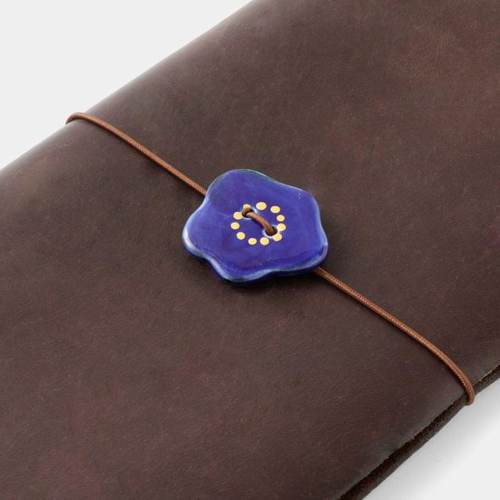 A brown leather-bound notebook with a blue button featuring a yellow floral design on the cover.