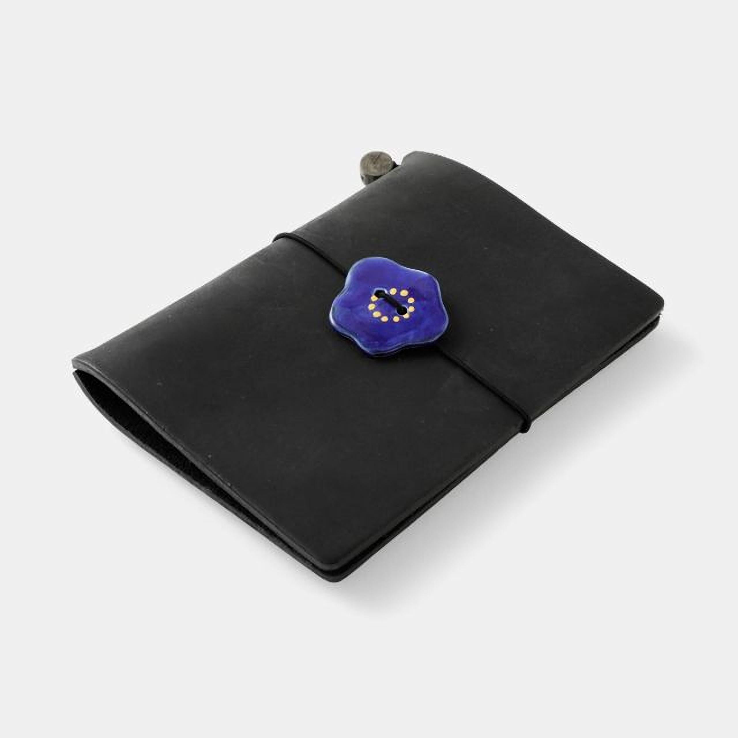 A black leather-bound notebook with a blue floral button on the cover.