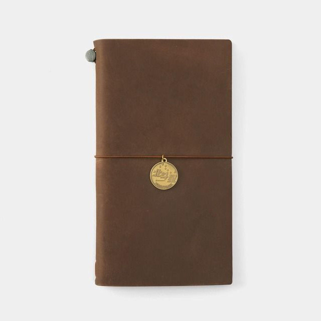 A brown leather-bound notebook with a gold-colored charm attached to the cover.