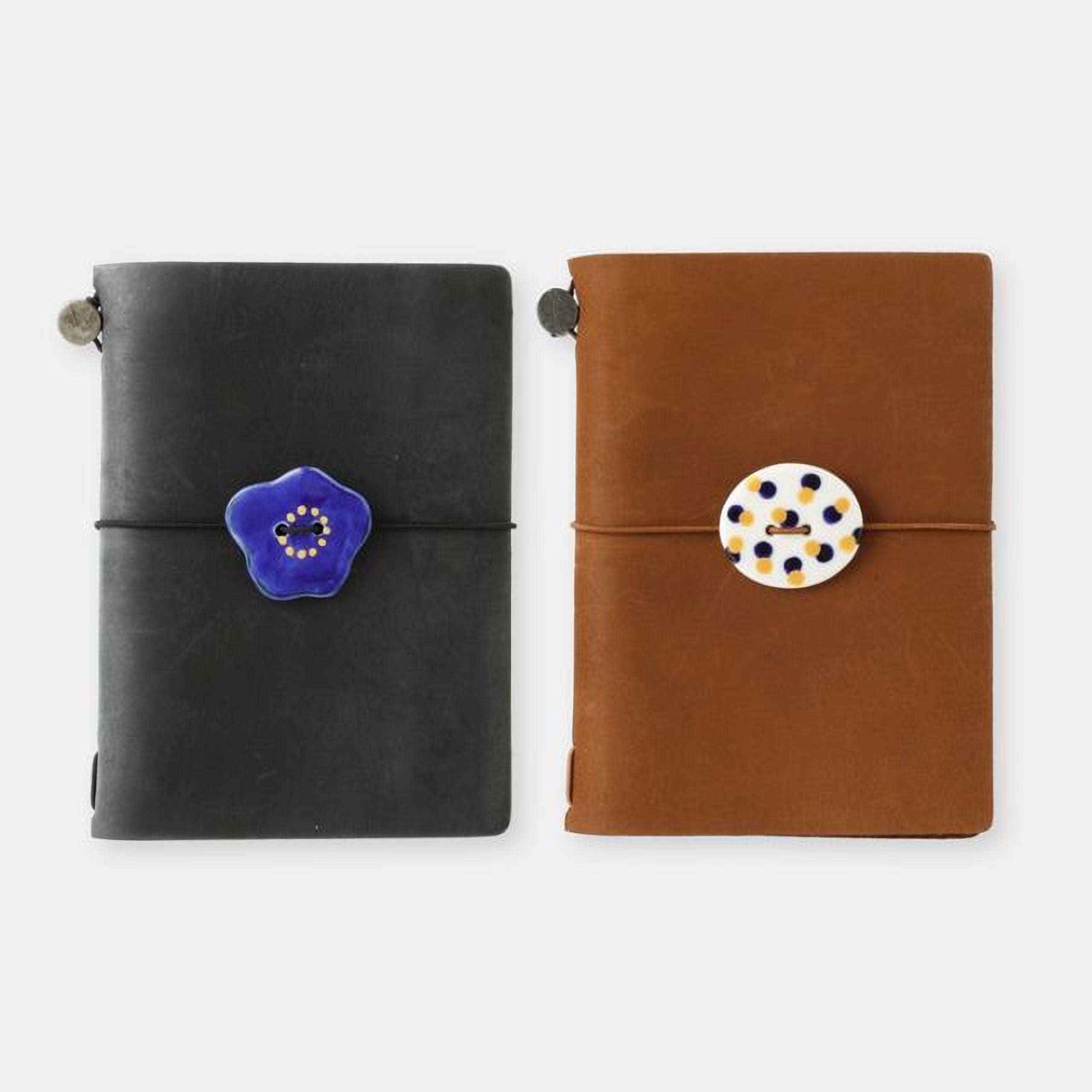 two notebooks with different colored bindings, one black and one brown, both with decorative buttons on the covers.