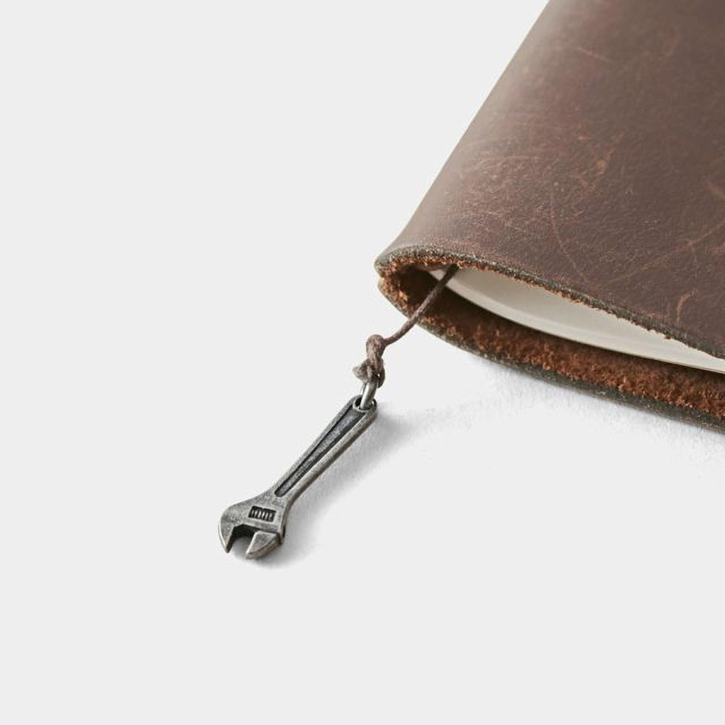 A close-up view of a brown leather-bound notebook with a metal wrench charm attached to the page.