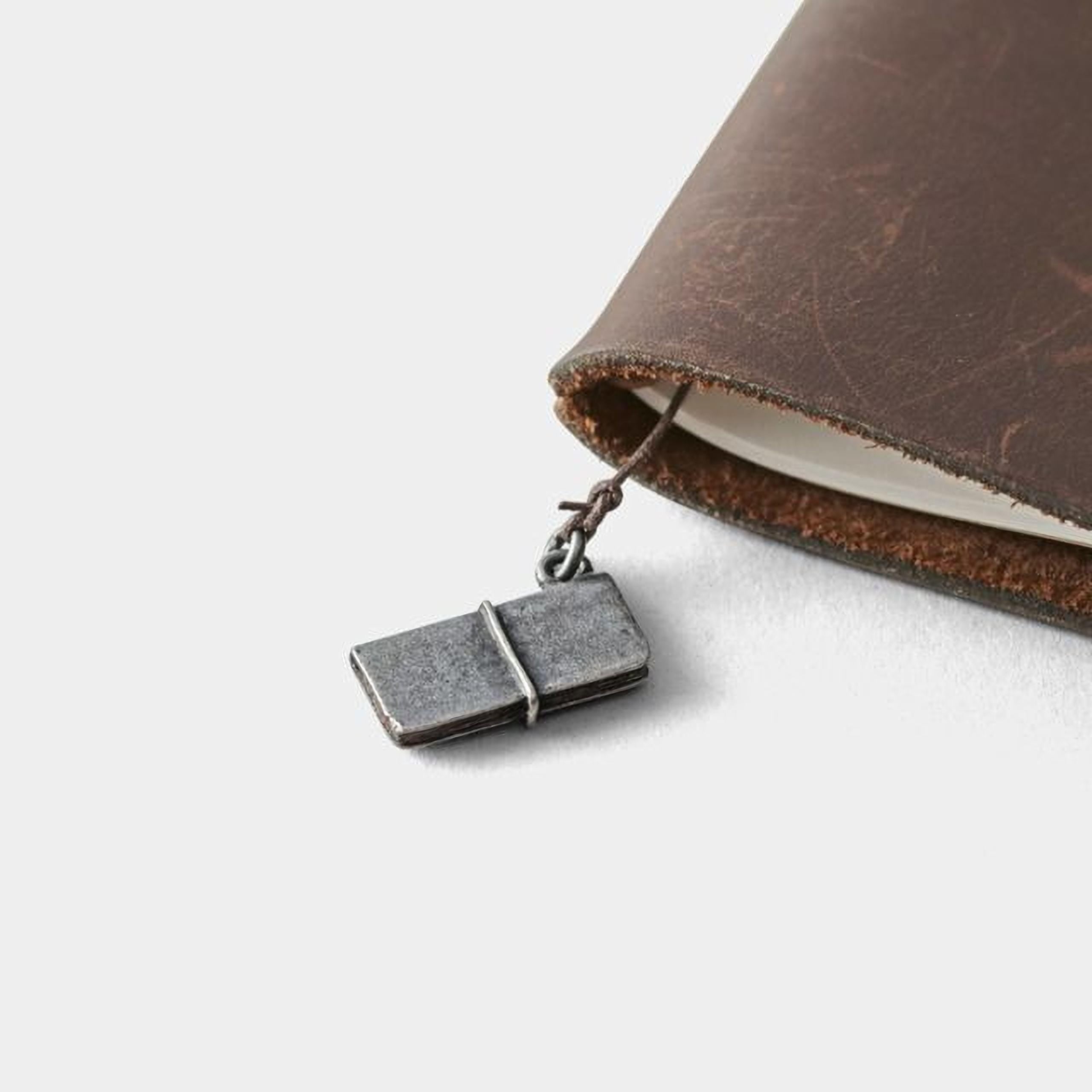 A small metal object, possibly a keychain or charm, is attached to the edge of a brown leather-bound notebook.