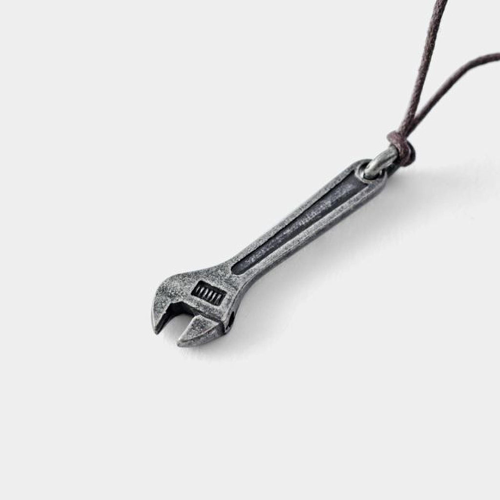 A silver wrench pendant with a leather cord attached, hanging against a plain white background.