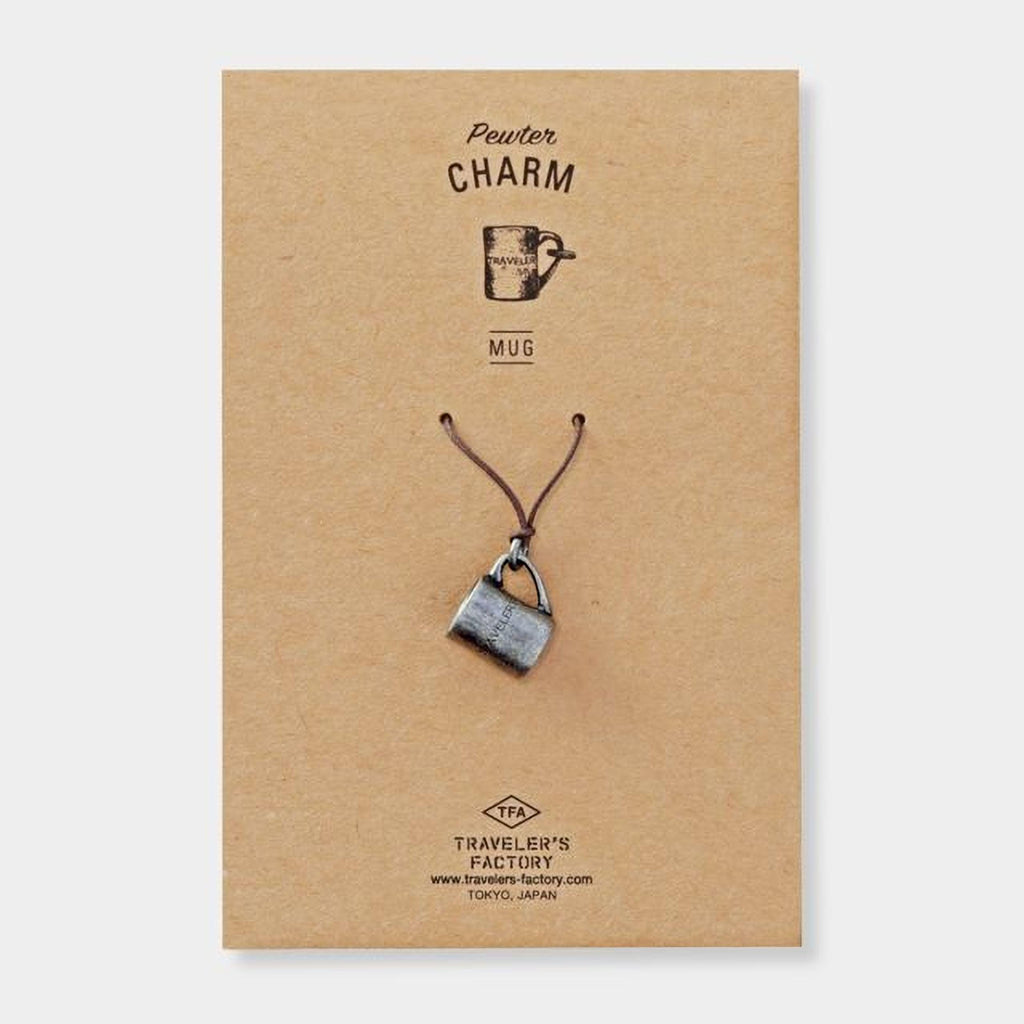 A charm made of a silver mug is displayed on a brown cardboard background.