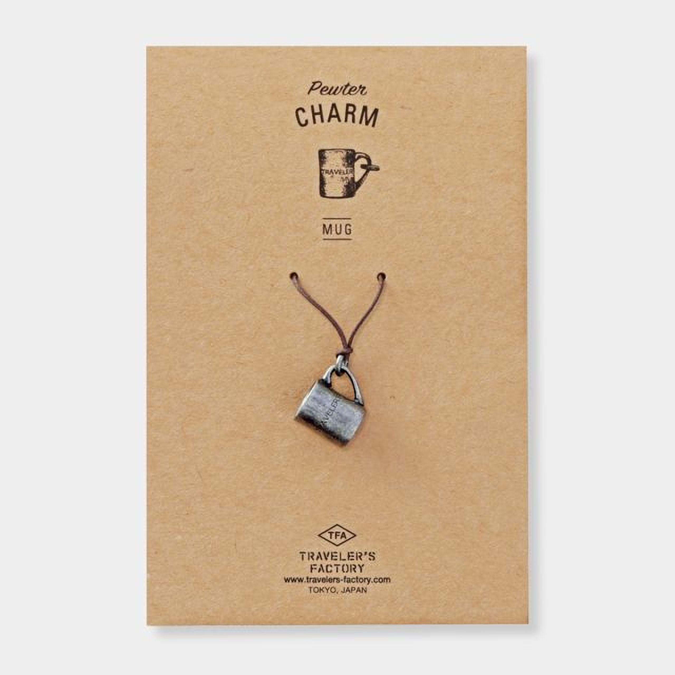 A charm made of a silver mug is displayed on a brown cardboard background.