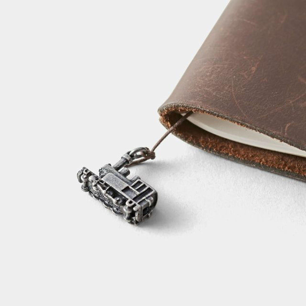 A small metal train charm is attached to a leather-bound notebook.