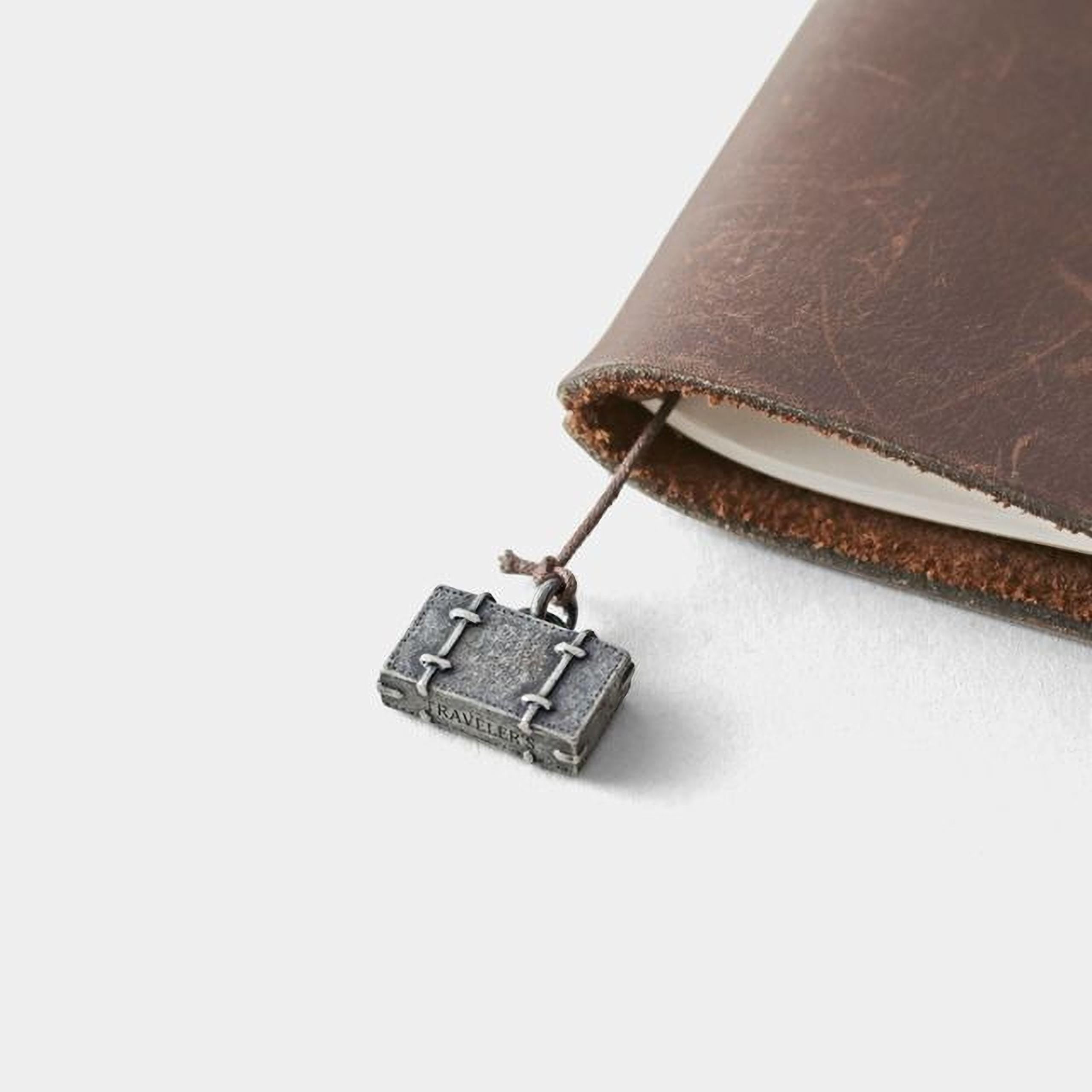 A small metal suitcase charm is attached to a leather-bound notebook.