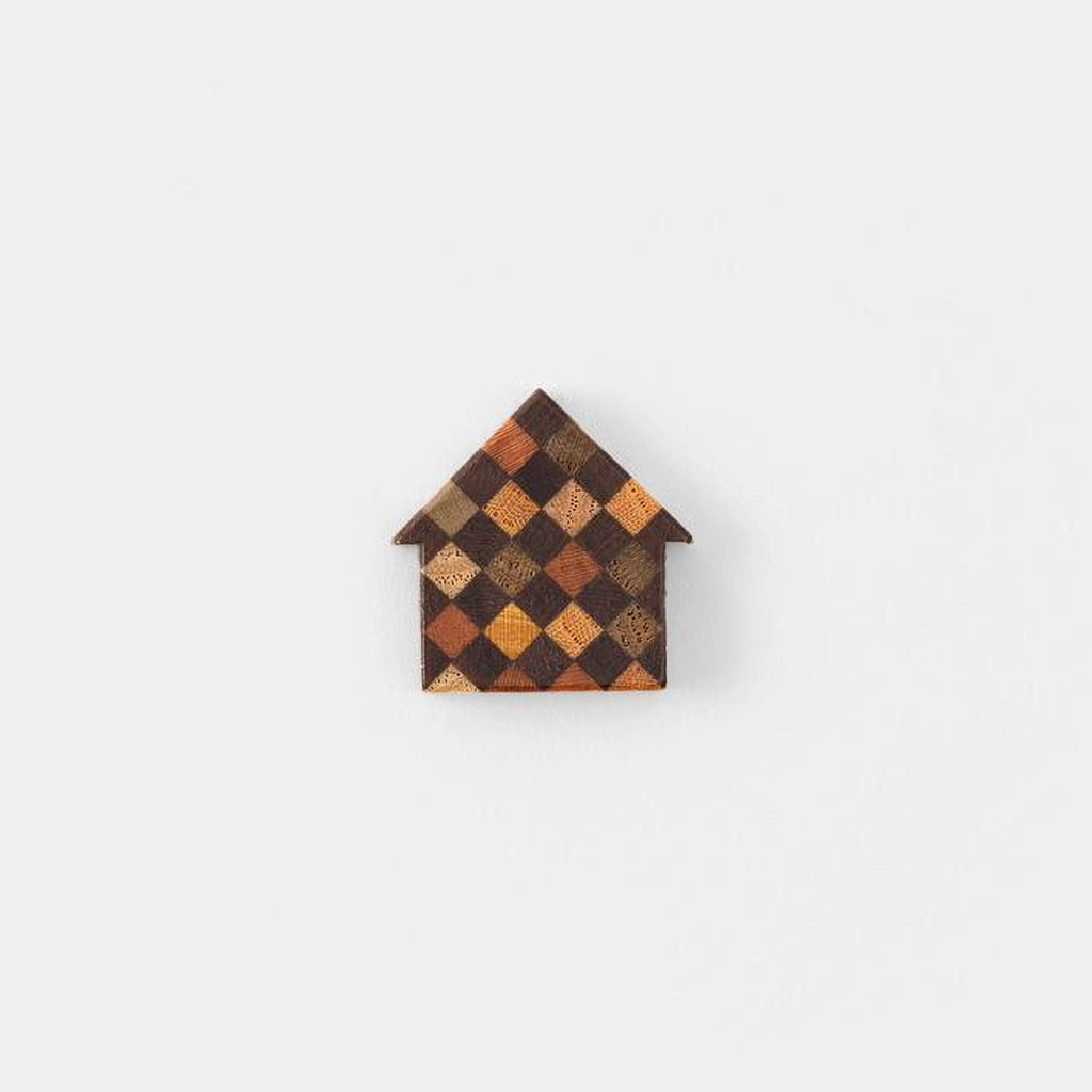 A small, colorful house-shaped object made of wood or another material, featuring a checkered pattern in various shades of brown and orange.