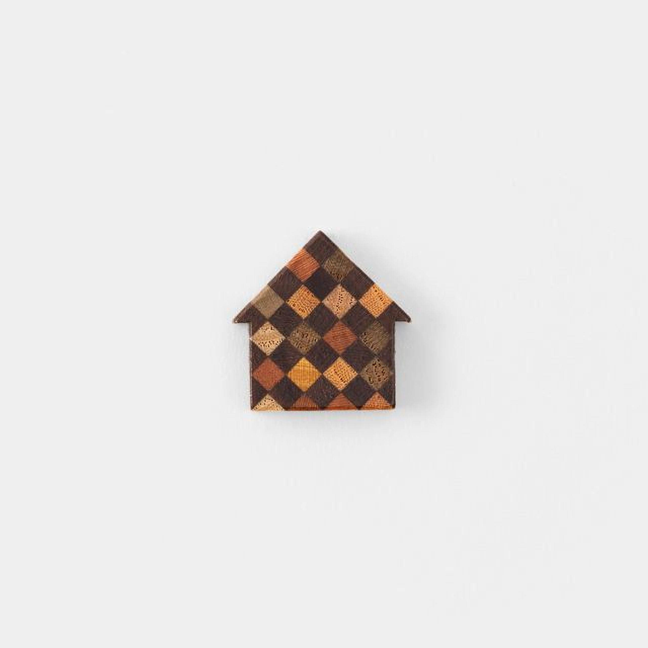 A small, colorful house-shaped object made of wood or another material, featuring a checkered pattern in various shades of brown and orange.