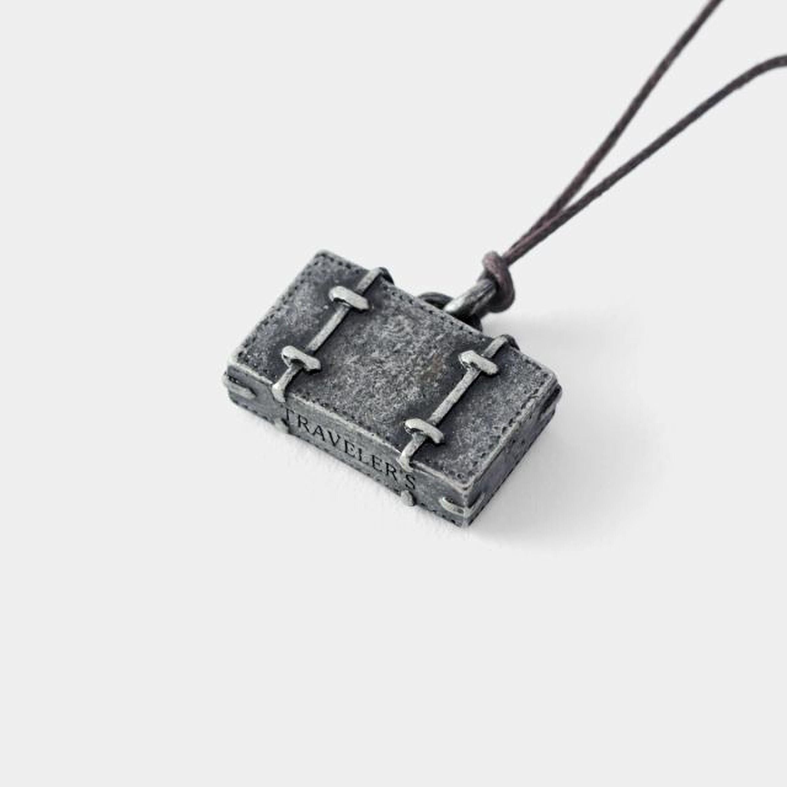 A small, rectangular pendant in the shape of a suitcase with the word "RAVELER" engraved on it.