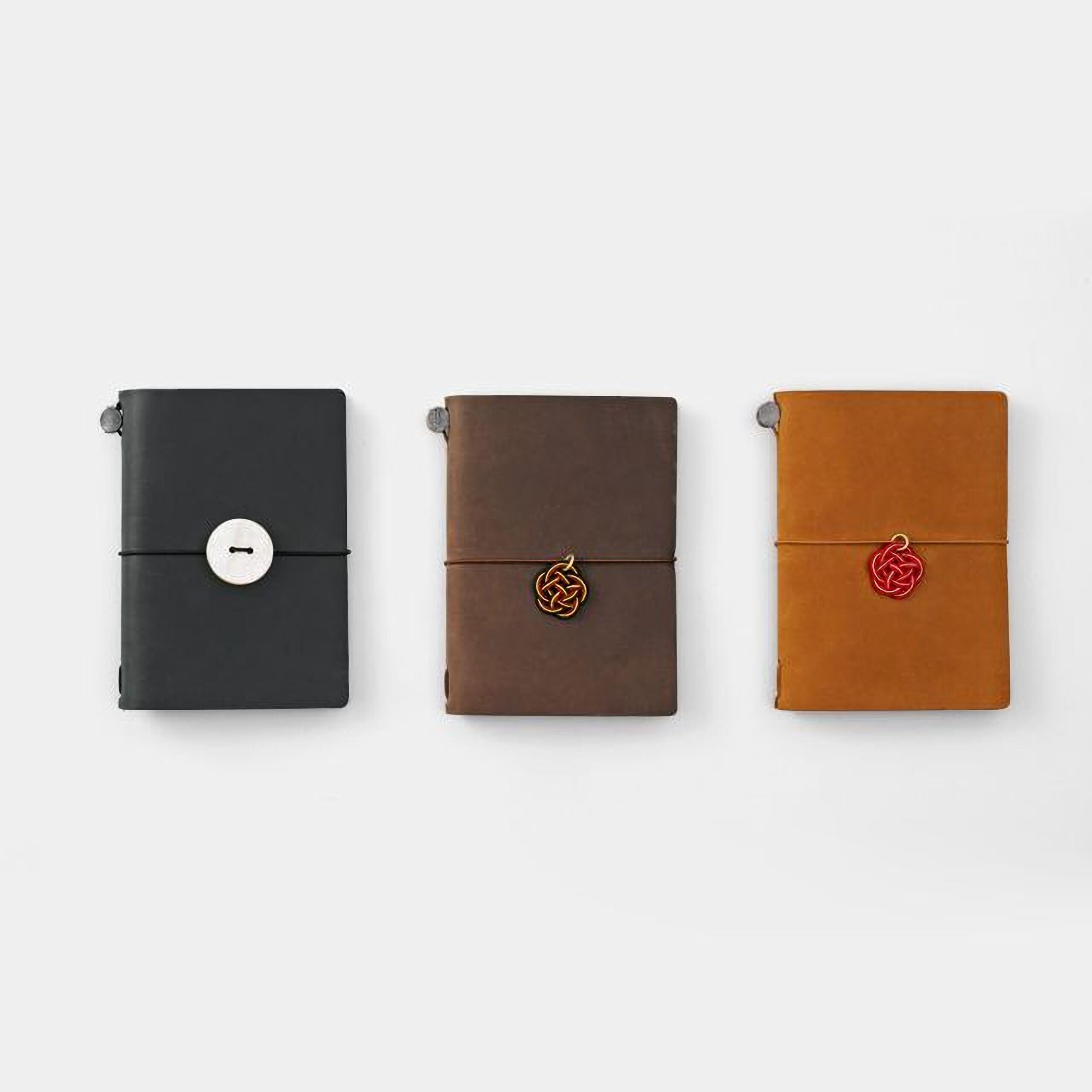 Three leather-bound notebooks in different colors - black, brown, and orange - are arranged in a row on a white background.