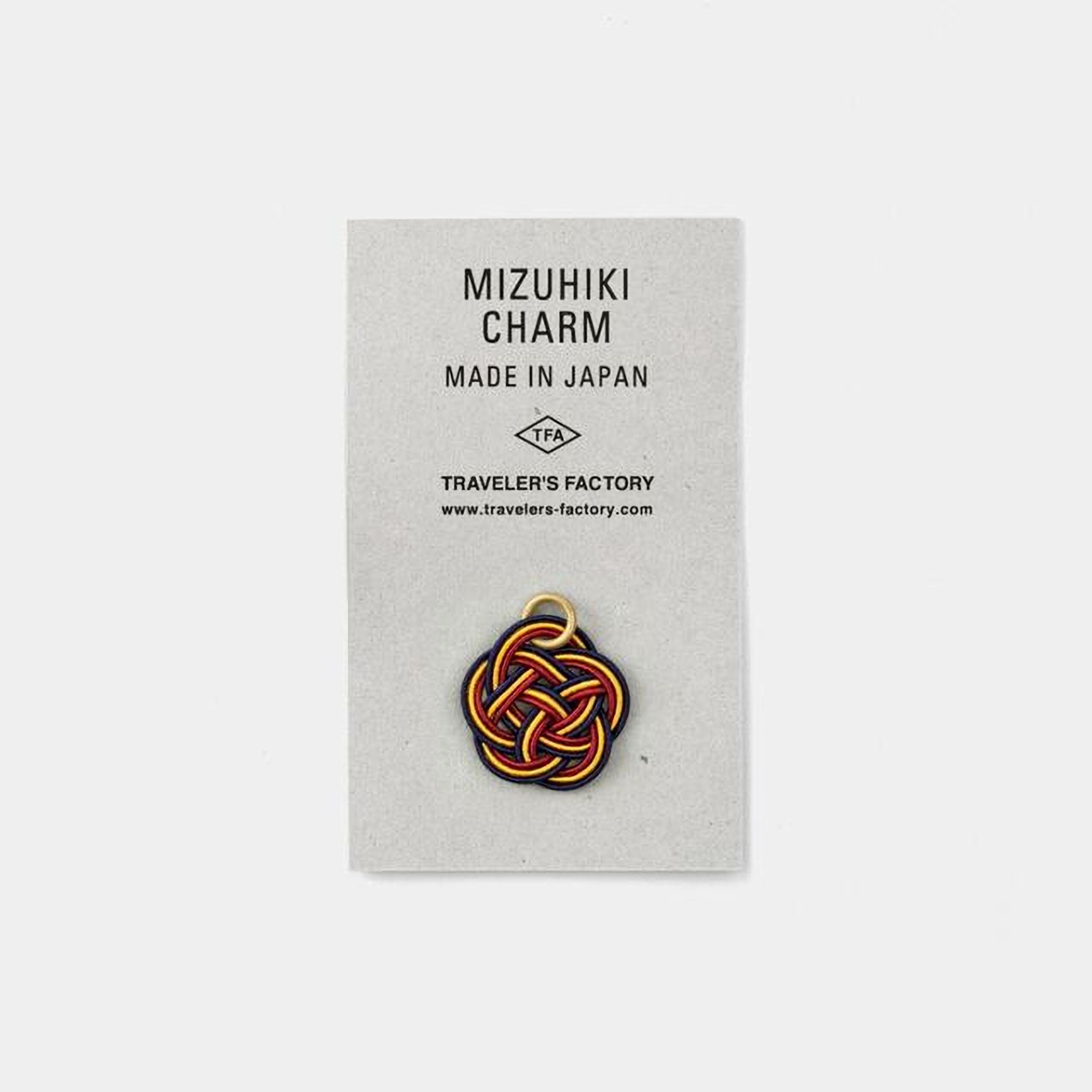 The image is a product advertisement for a charm, specifically the Mizuhiki charm, which is made in Japan. The charm is displayed on a gray background, and there is a website address provided for further information.