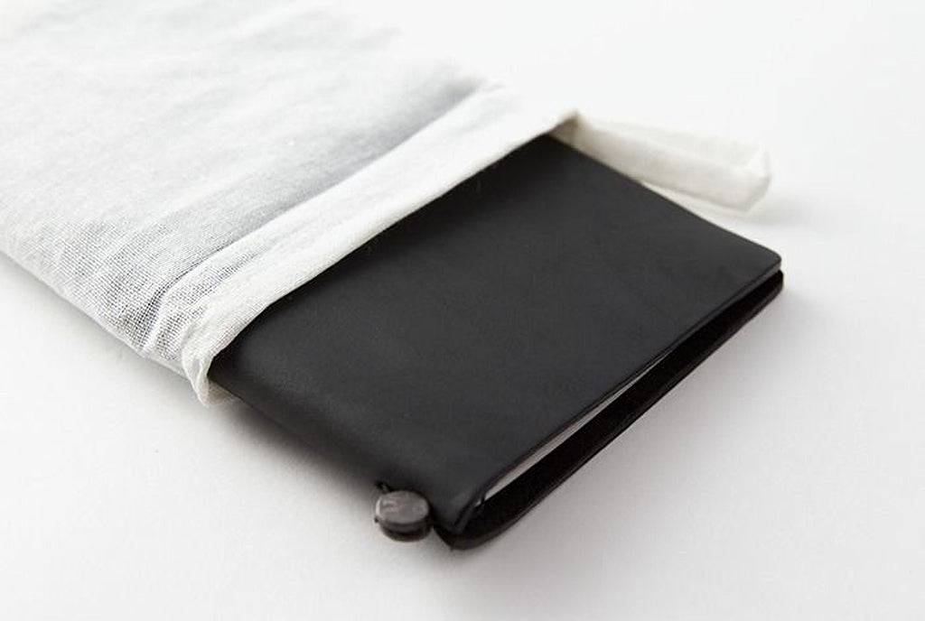A black leather-bound notebook or journal is shown, with a white cloth bag partially covering it.