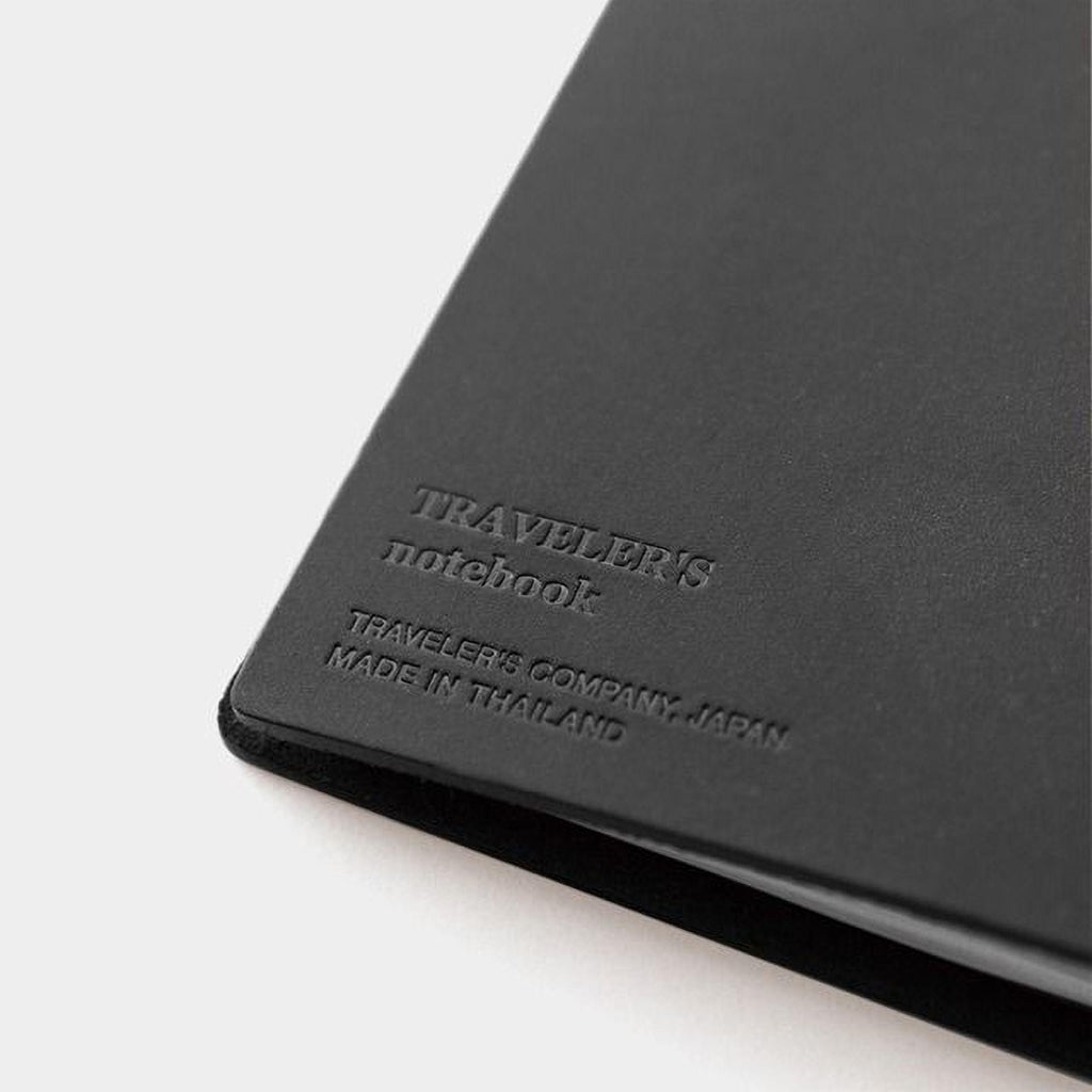A black leather-bound notebook with embossed text that reads "TRAVELER'S notebook" and "TRAVELER'S COMPANY, JAPAN MADE IN THAILAND".