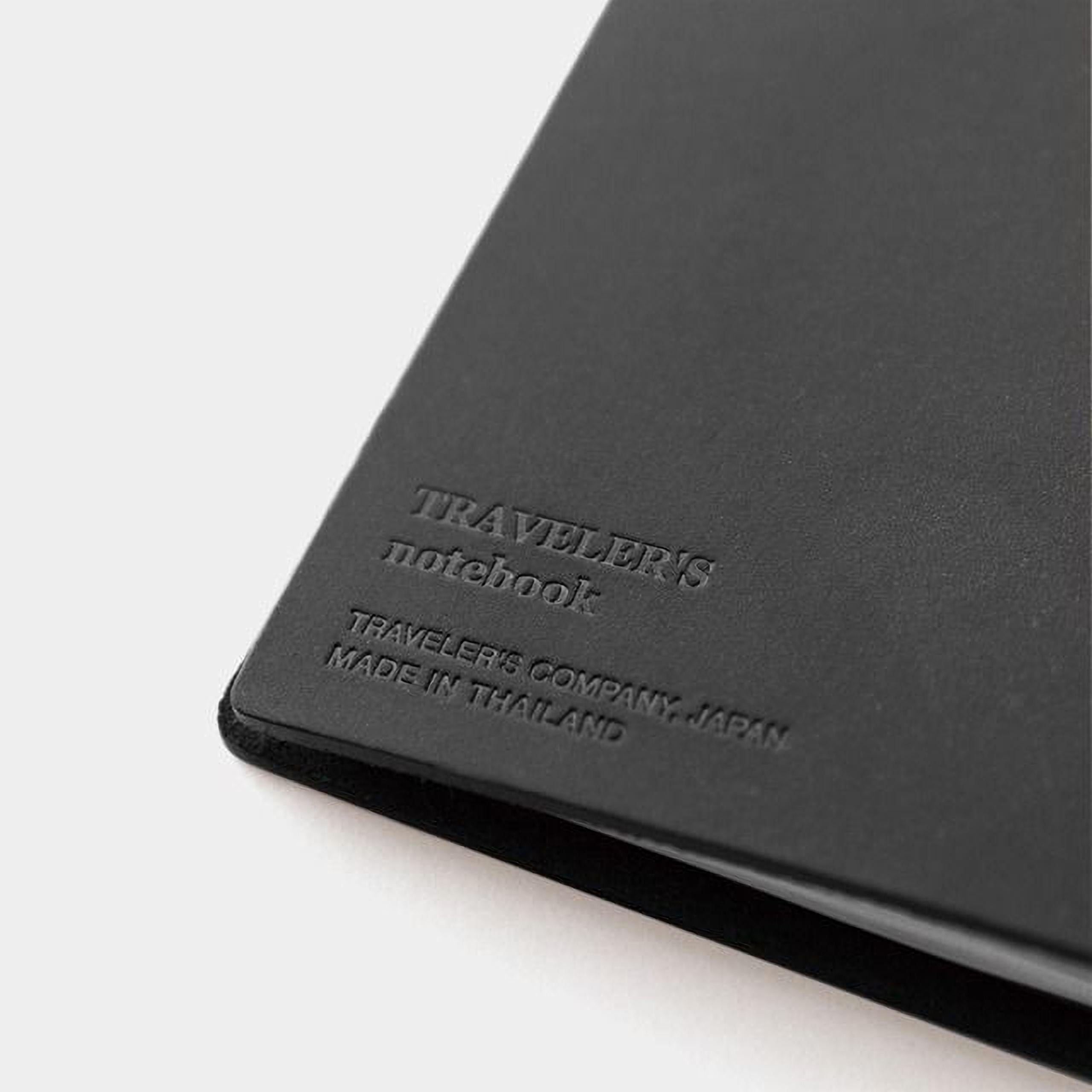 A black leather-bound notebook with embossed text that reads "TRAVELER'S notebook" and "TRAVELER'S COMPANY, JAPAN MADE IN THAILAND".