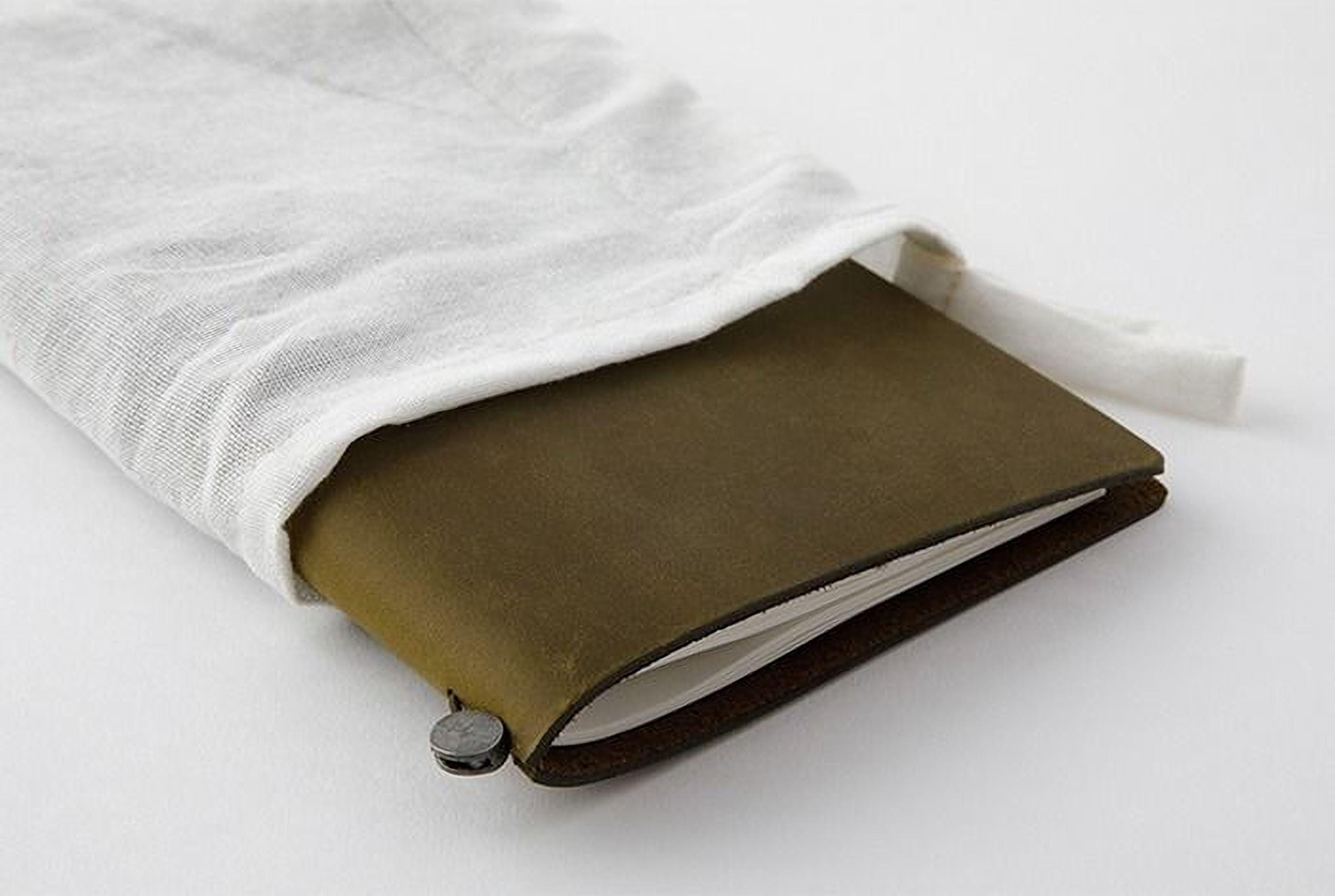 A brown leather-bound notebook with a white cloth draped over it, placed on a white surface.