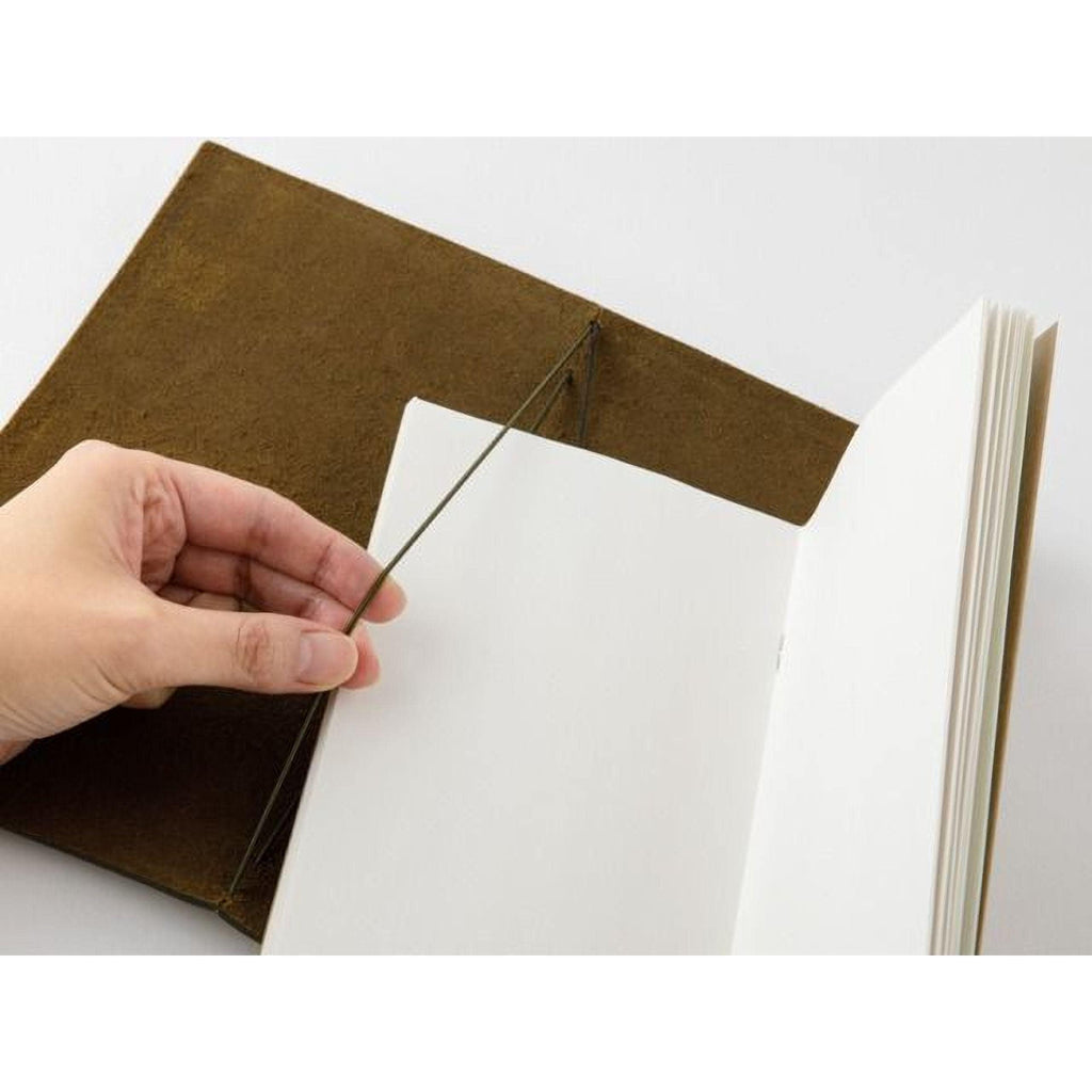A hand is holding open a brown leather-like object, which appears to be a notebook or book cover, with a white page inside.